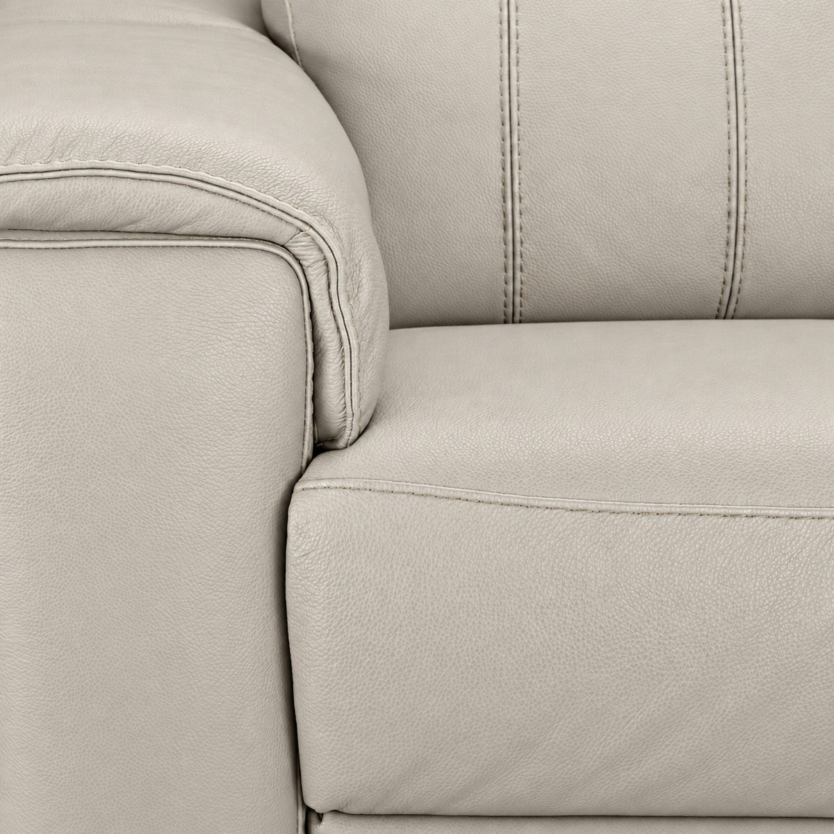 Close-up of cream leather grain, stitching, padded arm and seat cushion