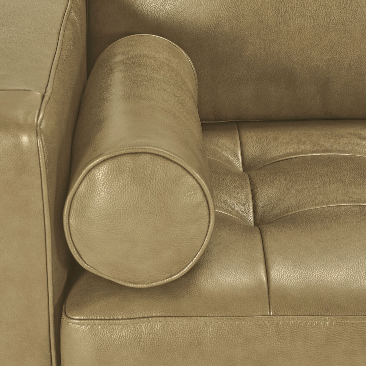 Close-up of Bari Leather Loveseat in stone showing a cylindrical bolster pillow, textured leather upholstery and tufted seat detail