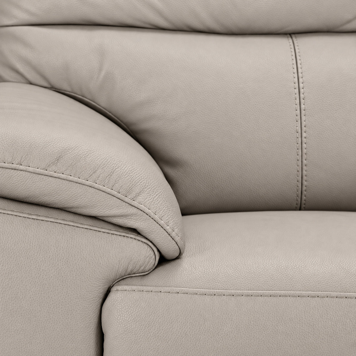 Close-up of light grey leather grain, stitching, padded arm and seat cushion
