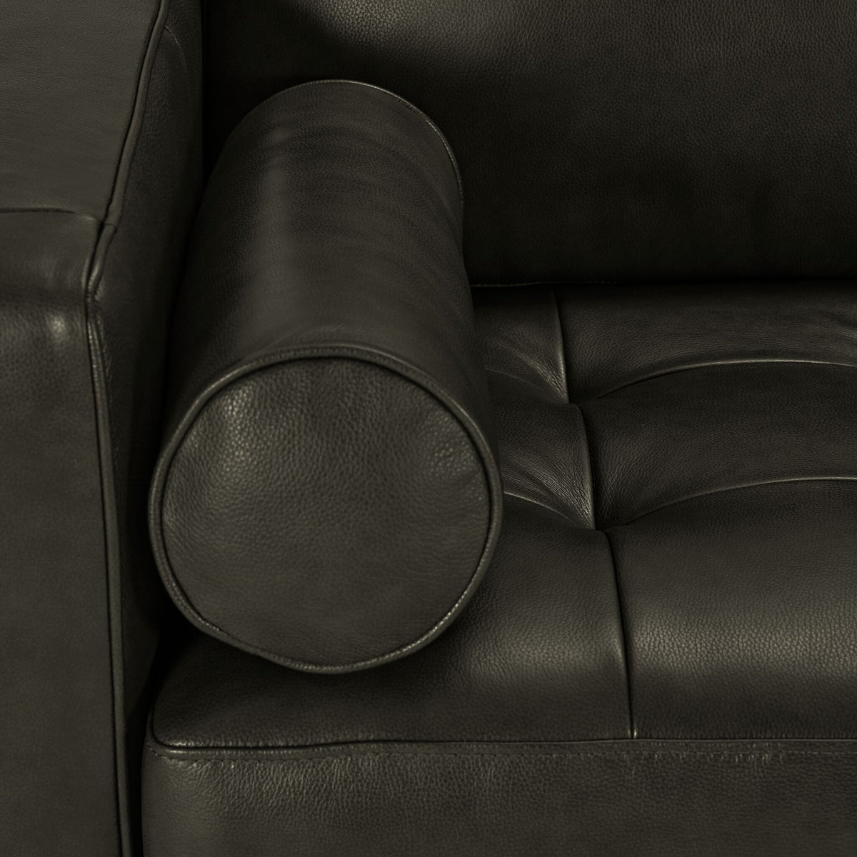 Close-up of charcoal leather upholstery with cylindrical bolster pillow, stitched edges and tufted seat cushion